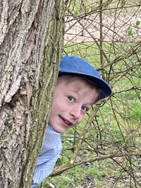 Ein Junge mit Kappe schaut hinter einem Baum hervor