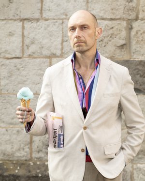 Portraitfoto von Eric Pfeil in weißem Sakko mit einem Eis in der Hand