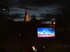 Eine Filmleinwand unter freiem Himmel im Restlicht der Dämmerung. Im Hintergrund die beleuchtete Stadtpfarrkirche Pfaffenhofen