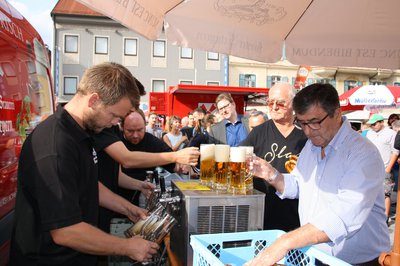 Bierzapfanlage, an der Bier gezapft wird, volle Bierkrüge, Sonnenschirme und Menschen in einer Schlange