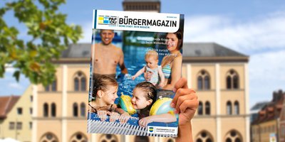 Hand hält das aktuelle Bürgermagazin in die Höhe. Im Hintergrund ist das Pfaffenhofener Rathaus zu sehen.