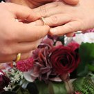Zwei Hände mit Ehenringen vor Blumenschmuck