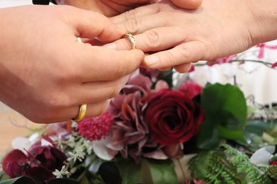 Zwei Hände mit Ehenringen vor Blumenschmuck
