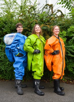 Drei Frauen in schicken Schutzanzügen mit viel zu großen Handschuhen