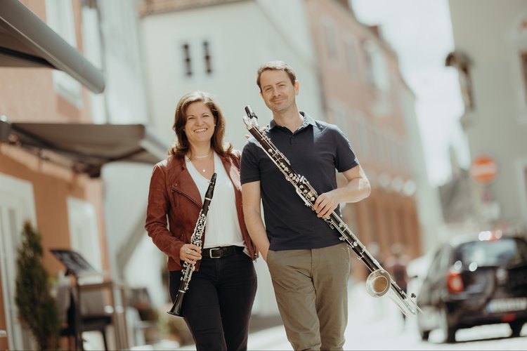Die beiden Musiker laufen mit ihren Instrumenten in der Innenstadt entlang.