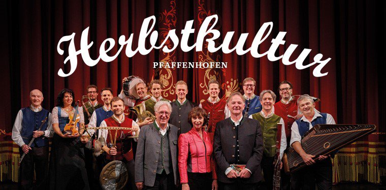 Schriftzug "Herbstkultur Pfaffenhofen" und viele Künstler mit ihren Instrumenten auf der Bühne vor einem roten Vorhang.